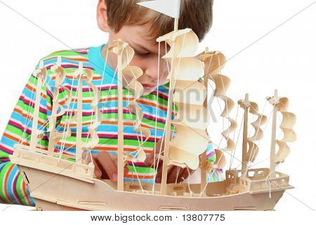 Small boy in striped shirt work with zeal on hull of artificial ship, focus on boat
