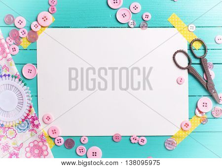Sewing thread - buttons scissors fabric and empty tag on turquoise wooden background. Selective focus. Scrapbboking. Flat lay. Place for text. Toned image.