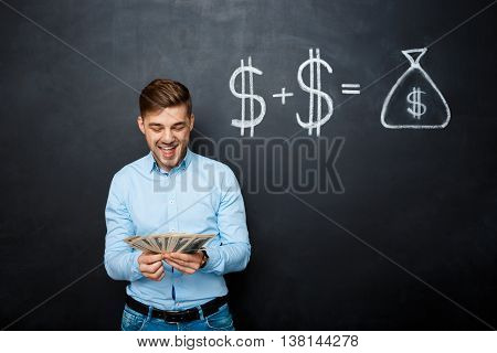 handsome man standing over blackboard. Holding dollars in his hands and smiling