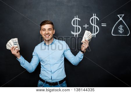 handsome man standing over blackboard. Holding dollars in his hands and smiling