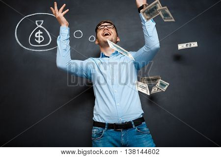 handsome man standing over blackboard. Holding and throwing dollars in his hands and smiling.