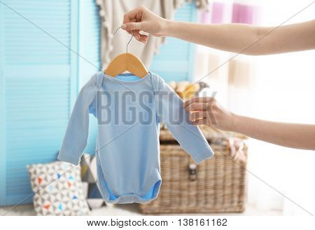 Female hand holding baby bodysuit in interior of child's room