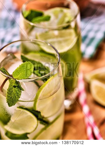 Alcohol drink. On wooden boards part of two glasses with lime alcohol drink and ice cubes. A drink number hundred eleven with two straw cocktails mohito and mint leaf. Country life. Light background.