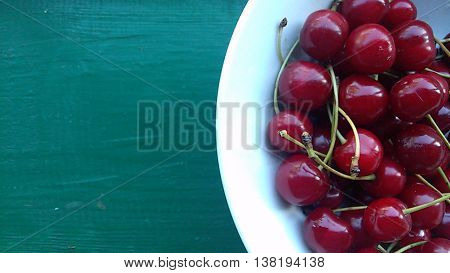 cherry in a bowl,  green background,  fresh berries