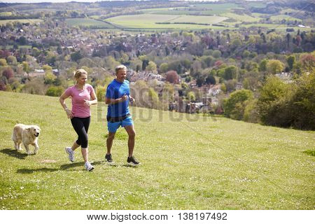 Mature Couple With Golden Retriever Jogging In Countryside