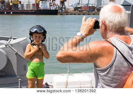 Odesa, Ukraine - July 03, 2016: Grandfather photographing a boy in a military helmet on new warship 'Akerman'. Celebration of Ukrainian NAVY forces day