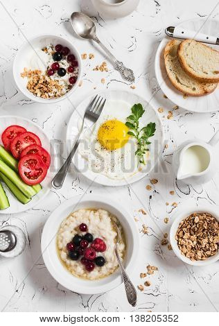 Assortment of breakfast - fried egg fresh vegetables oatmeal with berries cottage cheese yogurt and berries homemade granola on a light table. Healthy food. Top view