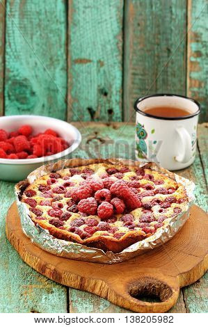 Homemade quark pie with raspberries in foil served on wooden board with green tea vertical