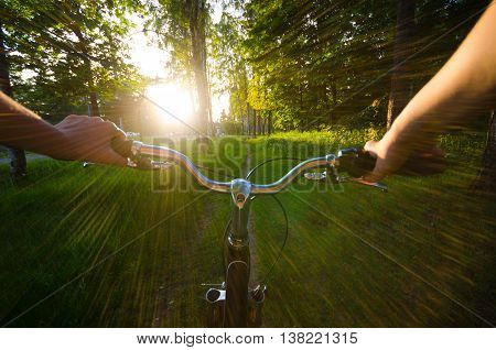 Eye view when girl ride by bycicle in park to sunset. Summer landscape. Sun goes down.
