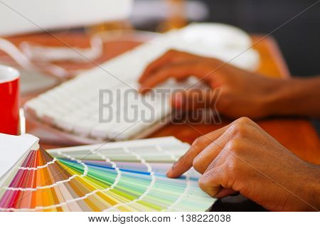 Closeup hands holding palette, colormap spread out in front of white computer keyboard, designer concept.