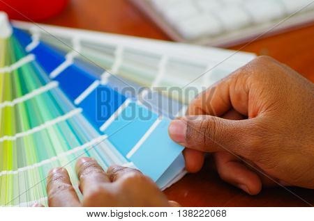 Closeup hands holding palette, colormap spread out in front of white computer keyboard, designer concept.