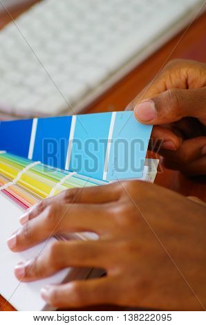 Closeup hands holding palette, colormap spread out in front of white computer keyboard, designer concept.