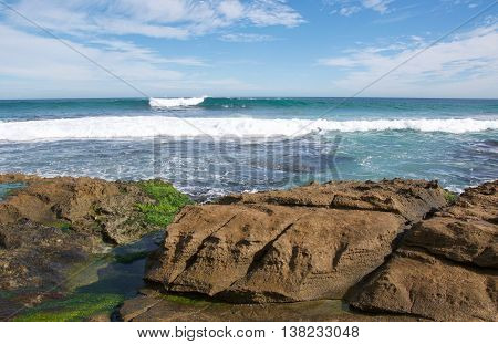 Algae covered limestone and turquoise Indian Ocean waters under a blue sky with clouds at Penguin Island in Rockingham, Western Australia.