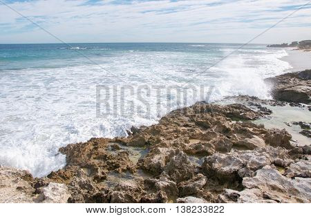 Foamy Indian Ocean waves with seascape under a blue sky with clouds at Penguin Island's remote, rocky beach in Rockingham, Western Australia.