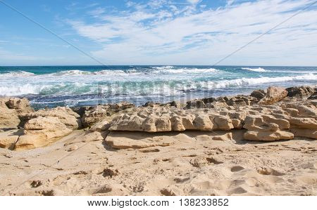 Rugged limestone coast with turquoise Indian Ocean waters under a blue sky with clouds at Penguin Island in Rockingham, Western Australia.