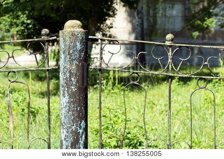A fence made of rusty metal rods. Very old and rusty. A long time outdoors. The background is blurred (green grass).