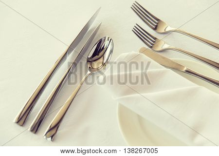 table setting, silverware and eating concept - close up of cutlery set wrapped with napkin and plate on restaurant table