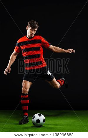 Soccer player in black and red uniform kicking ball on grass over black background
