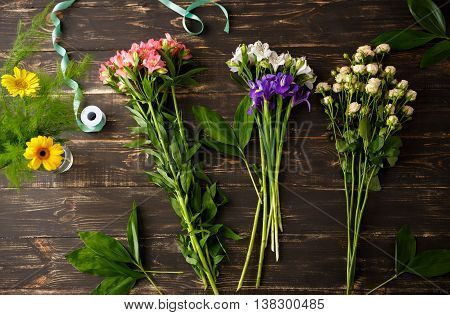 Bright colorful irises, roses, leaves and  alstroemerias on wood table, herberas in vase. From above.
