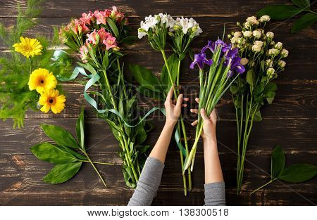Bright colorful alstroemerias and irises in hands, roses on wood table, herberas in vase. From above.