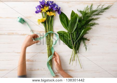 Bright colorful irises, herberas and alstroemerias with green ribbon in hands on wood table. From above.