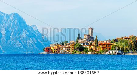 Ancient tower and fortress in old town malcesine at garda lake veneto region italy high snowbound top mountains on background summer landscape with colorful houses green trees