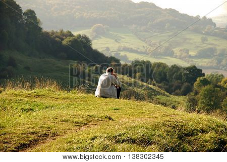 Tourist sit on peak of hill and watching into colorful valley. Sad man. Man sit. Fall mountain mist. Sad tourist sit in mist.