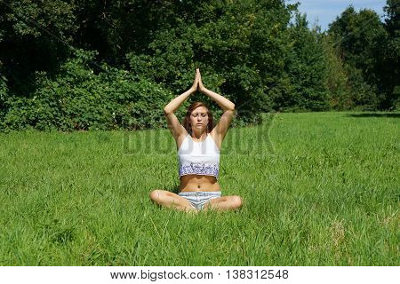 young woman practicing yoga meditation outdoors in a meadow