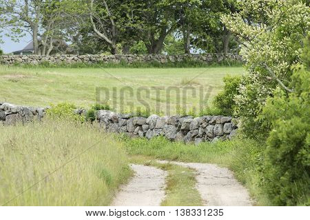 Dirt road through field diverted by New England stone wall