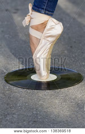 Foot girls in puante stands on a vinyl disc, which lies on the road.