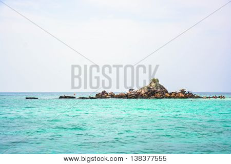 A small island called Koh Kai in Phuket surround with clear blue water and partly cloud sky.