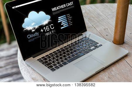technology, weather cast, business and modern life concept- close up of open laptop computer with meteo forecast on screen on table at hotel terrace