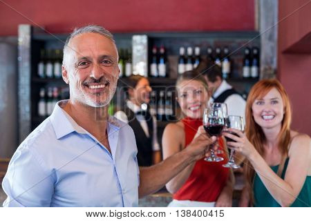 Portrait of friends toasting with a glass of red wine at bar counter in a bar