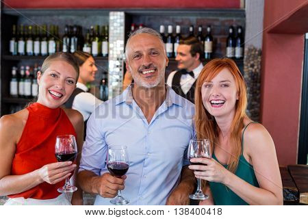Portrait of happy friends standing at bar counter with a glass of red wine in bar
