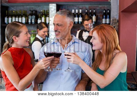 Friends toasting with a glass of red wine at bar counter in a bar