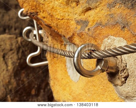Detail of steel anchor eye and rope end anchored into sandstone rock. Iron twisted rope fixed in block by screws snap hooks.  Trekking via ferrta.