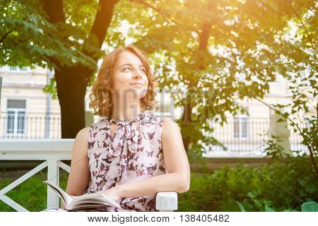 Portrait of caucasian young woman in summer dress on park bench. Image with lens flare effect