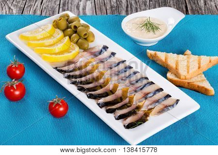 fish appetizer - slices of smoked and marinated mackerel on rectangular dish with sliced lemon green olives tomatoes toasts and horseradish close-up