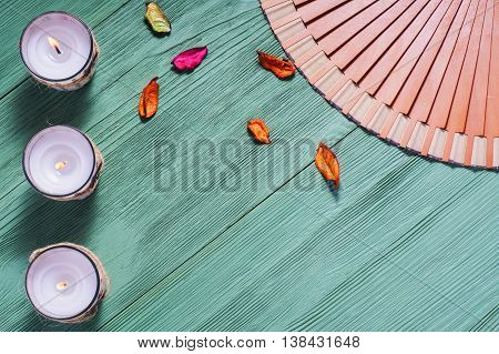 Zen candle and fan with hieroglyphs on a green wooden background close up. Spa concept flat lay.