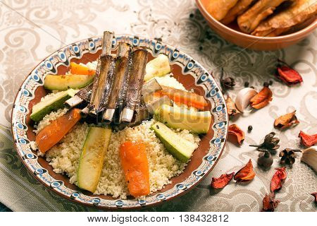 Traditional couscous dish with lamb ribs and vegetables. Still life with rose petals on the table. The image is describing moroccan culture