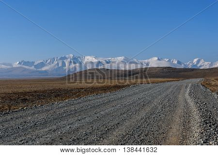 Scenic steppe landscape with a gravel road in the steppe mountains covered with snow and hills against the blue sky on a sunny day