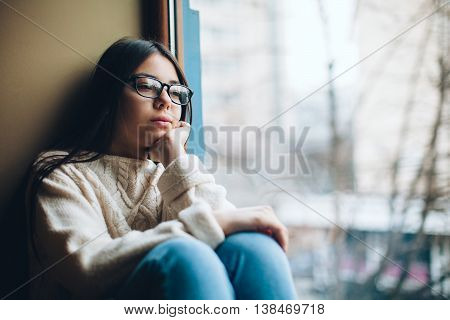 Sad teenage girl looking out the window on a cold autumn day