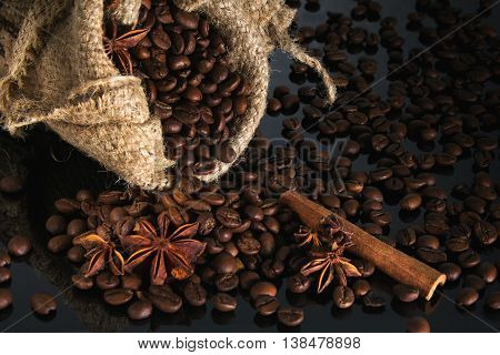 coffee grains into the sack and scattered on a black background with an anise and cinnamon