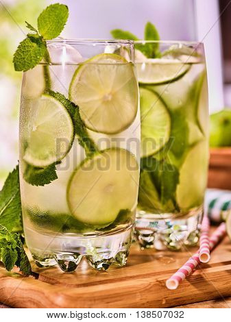 Alcohol drink. On wooden boards two glasses alcohol drink and ice cubes. Close up of drink number hundred fifty seven cocktail mohito with straw and lime and mint leaf. Country life. Light background.