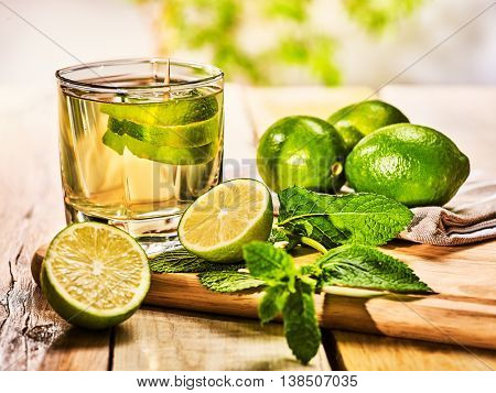 Alcohol drink. On wooden boards glass with alcohol green mohito drink. Mint drink number hundred fifty four mojito cocktail with half lime and napkin. Country still life outdoor. Light background.