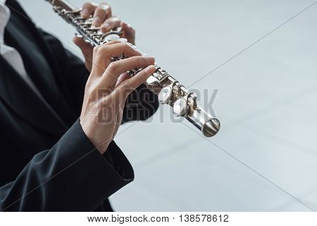 Professional elegant female flutist performing in a white room hands close up