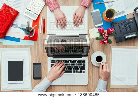 Coworkers sharing the same desk with customized workspace and working with a laptop top view