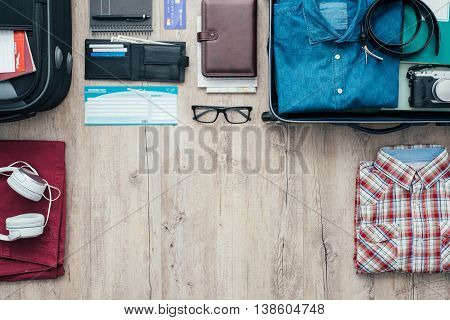 Getting ready for a trip and packing a suitcase before leaving; accessories clothing and personal items on a desktop travel and vacations concept