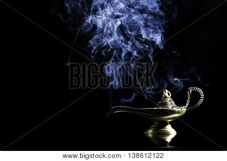 Magic lamp on black background from the story of Aladdin with Genie appearing in blue smoke concept for wishing, luck and magic