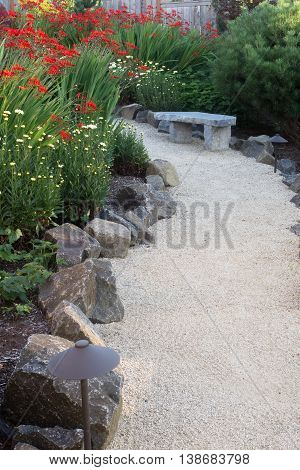 A curved garden path edged with stones winds through a perennial garden with crocosmia and dasies.